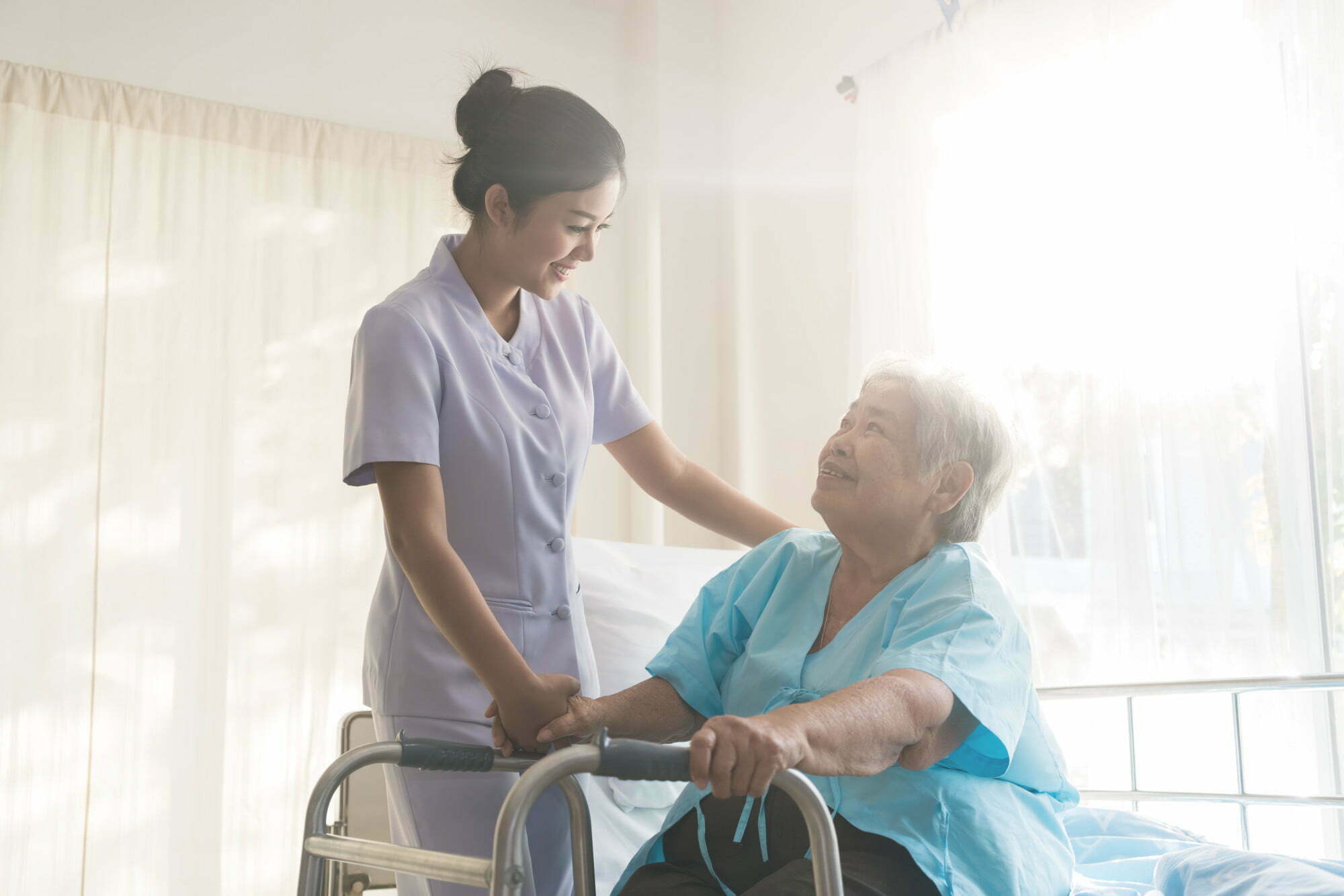 Asian young nurse supporting elderly patient disabled woman in using walker in hospital. Elderly patient care concept.